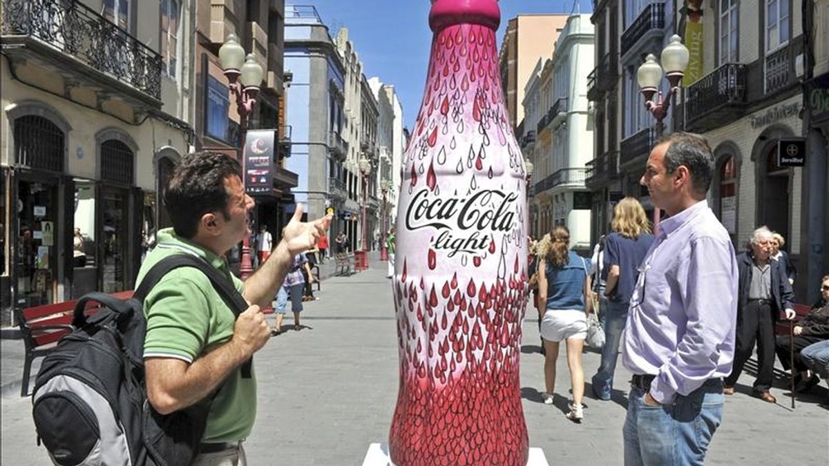 Dos hombres observan una de las siete botellas gigantes de Coca Cola light decoradas por otros tantos diseñadores españoles instaladas en Las Palmas de Gran Canaria. EFE/Archivo