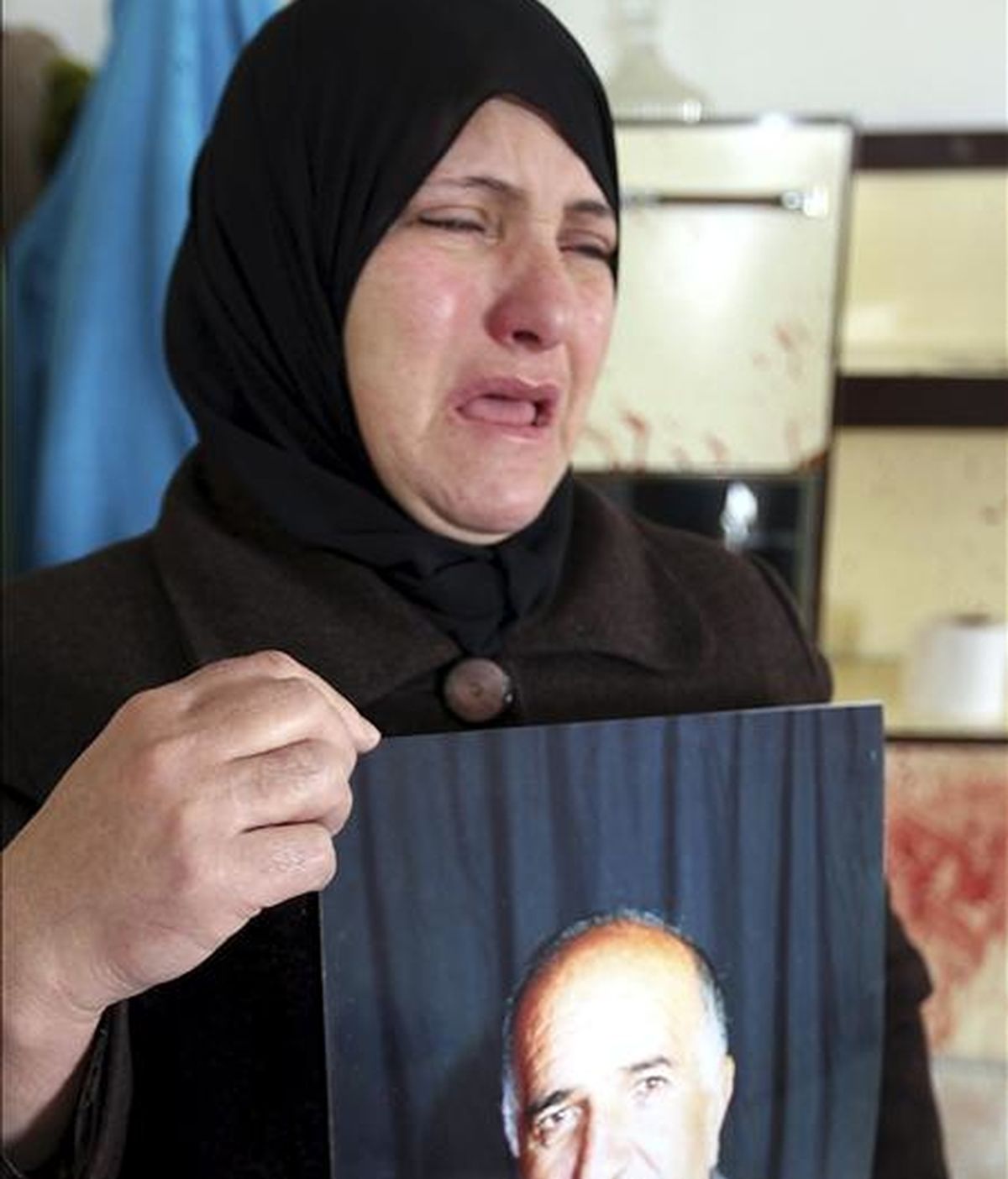 La esposa de Omar Kawasme (67 años) sostiene su fotografía mientras que, en el fondo, se proyecta la cama manchada con sangre, donde fue asesinado por las tropas israelís durante un ataque para arrestar a presuntos milicianos, según alega su esposa hoy, 7 de enero de 2011, en Hebrón. EFE