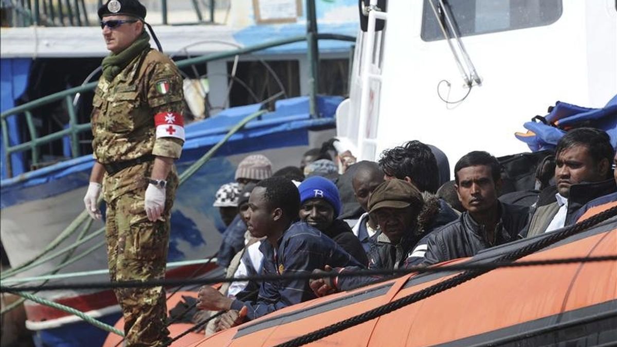 Inmigrantes subsaharianos a bordo de un bote que partió de Misurata, Libia, hace cuatro días son custodiados mientras llegan al puerto de la isla italiana de Lampedusa. EFE