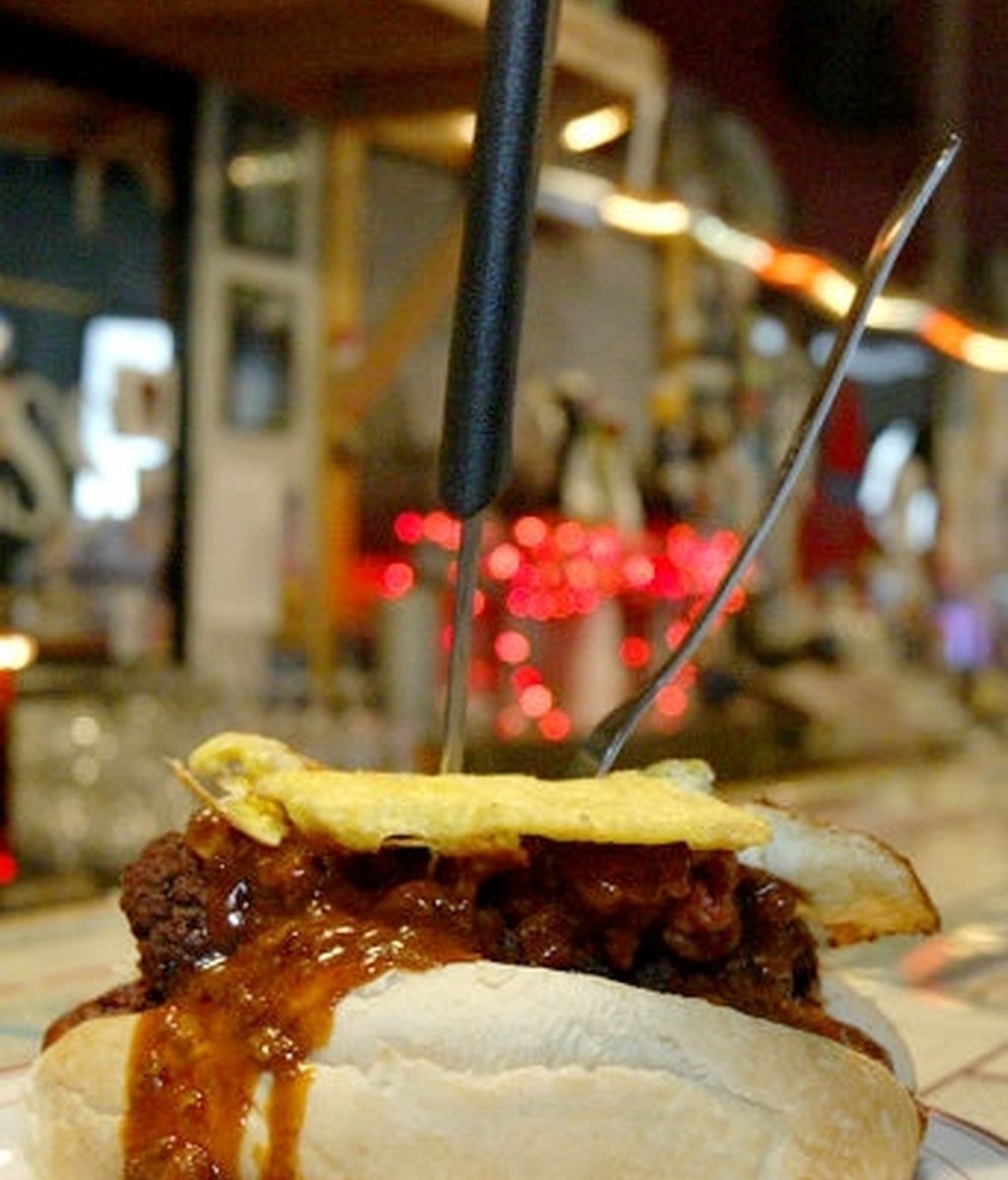 Perrito caliente dentro de una hamburguesa con chile y cebolla, huevo frito, y pan. Acompañado con patatas fritas