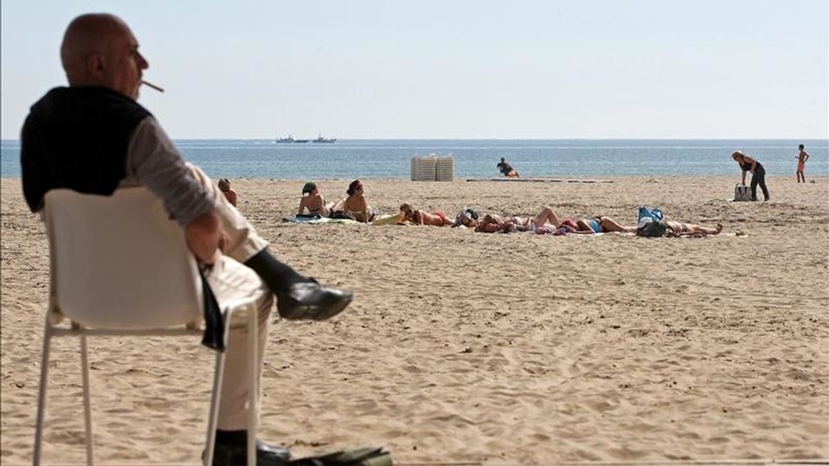 Un grupo de mujeres toma el sol este mediodía en la playa de Las Arenas de Valencia mientras un hombre fuma un cigarrillo sentado en le paseo marítimo. EFE