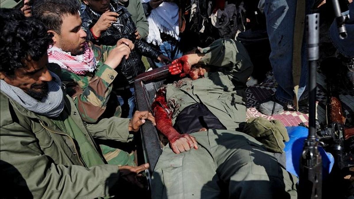 Soldados rebeldes libios toman fotografías de un soldado leal al líder libio Muamar el Gadafi que resultó herido, en la parte trasera de un vehículo, en la carretera entre Brega y Ajdabiya, en Libia. EFE