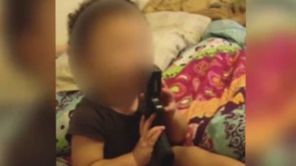 Un bebé se mete una pistola en la boca alentado por sus padres