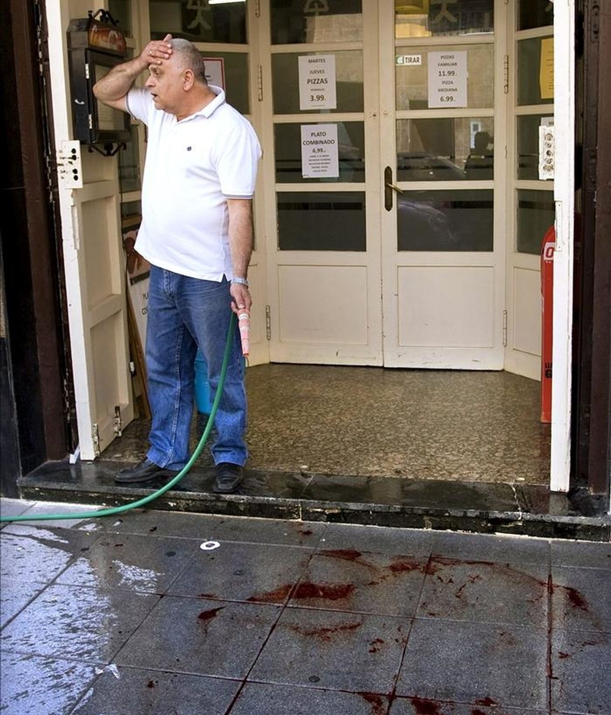 Un hombre limpia restos de sangre ante su establecimiento, en el lugar en el que murió apuñalada, presuntamente, por su pareja en Almería. EFE