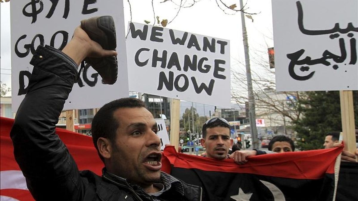 Manifestantes libios gritan consignas y ondean banderas mientras protestan en las afueras de la embajada de Libia, en Atenas, Grecia. EFE