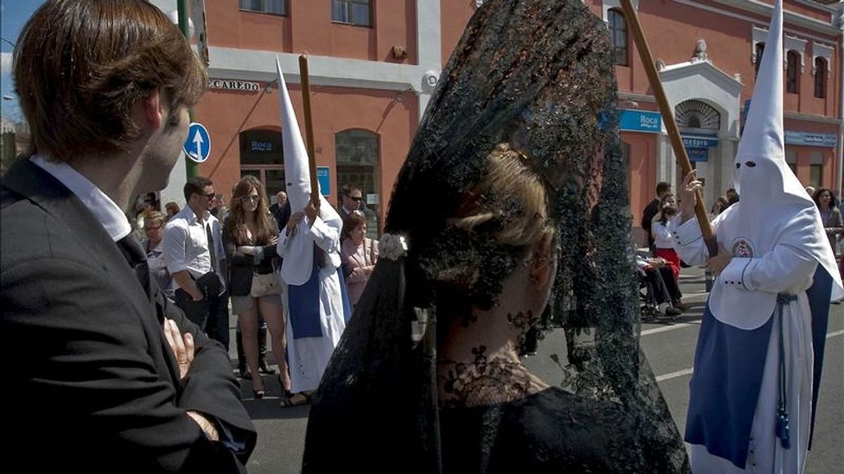 Una mujer atavíada con la típica mantilla, entre las personas que observan el paso de los nazarenos de la Hermandad de Los Negritos por las calles centricas de Sevilla. EFE/Archivo