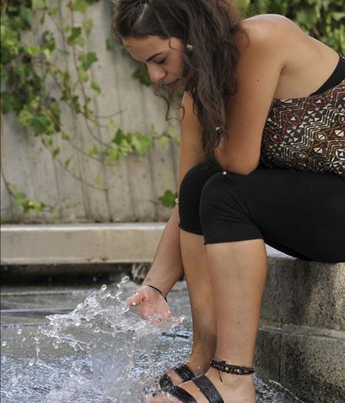 Una joven se refresca el agua de una fuente de la plaza de Tirso de Molina de Madrid, para intentar sofocar las altas temperaturas que se registran en la capital. EFE