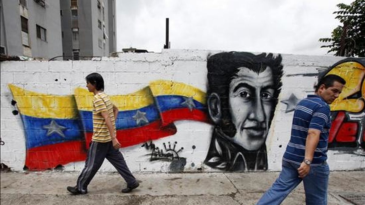 Fotografía en la que aparecen dos jóvenes mientras caminan frente a un mural con la imagen de Simón Bolívar en Caracas (Venezuela). EFE