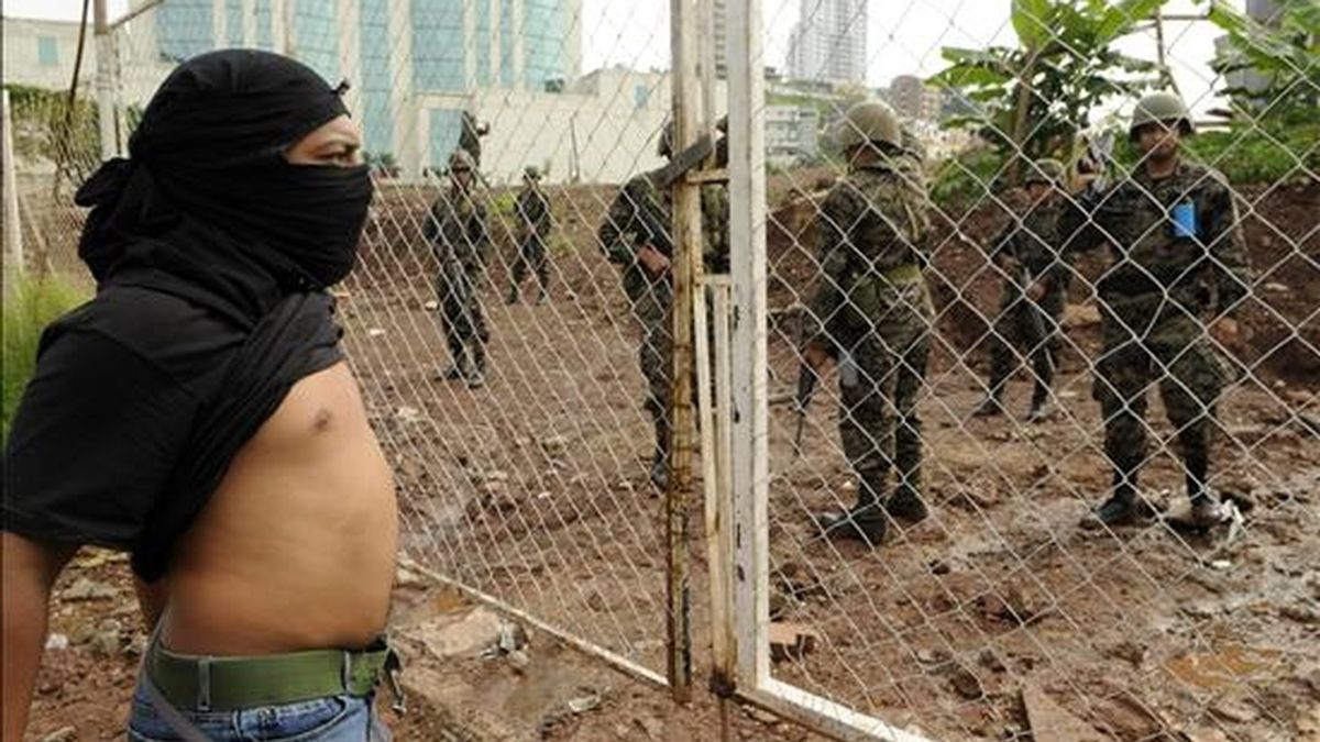 Manifestantes encapuchados se concentran frente a la Casa Presidencial, en Tegucigalpa (Honduras), ante la vigilancia de miembros del ejército. EFE