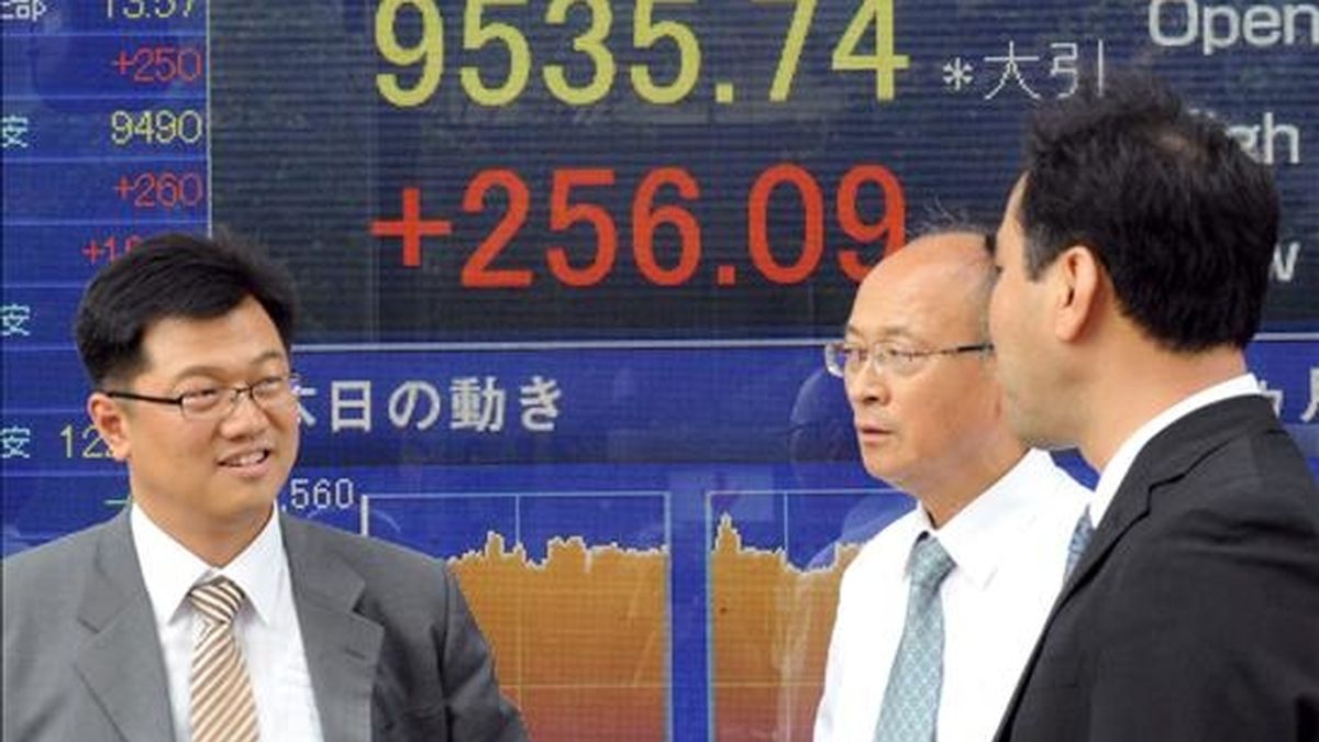 Tres hombres de negocios japoneses conversan ante una pantalla en la que aparece el índice Nikkei, en el centro de Tokio (Japón). EFE/Archivo