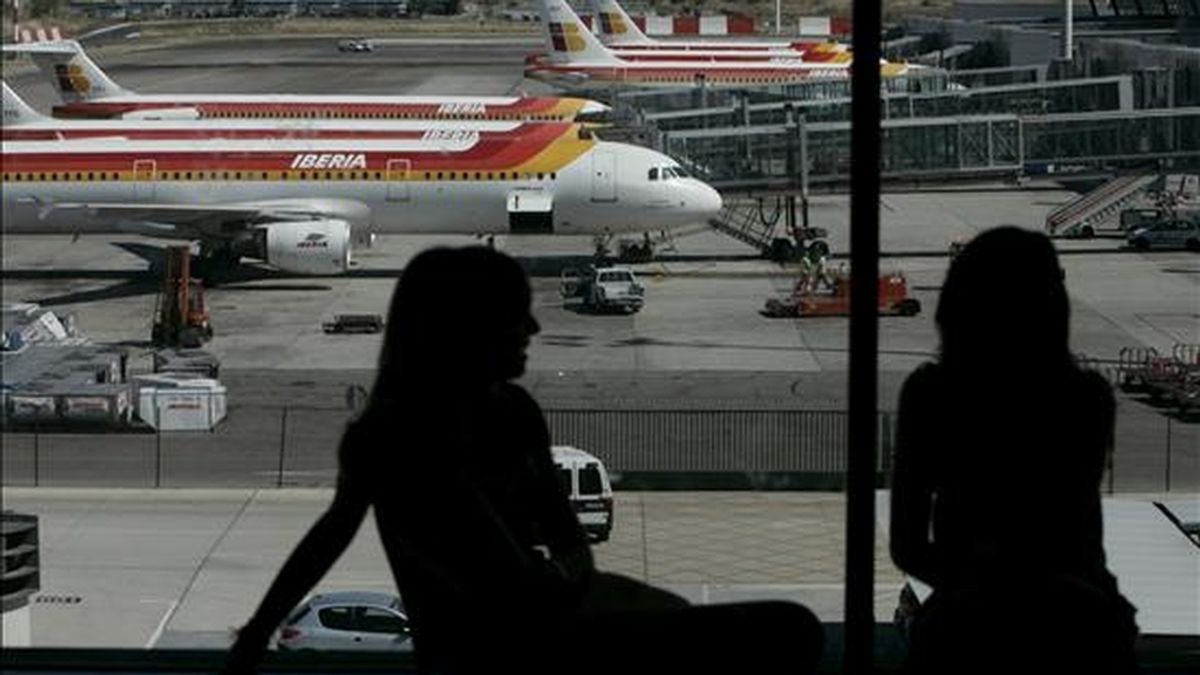 Dos jóvenes conversan frente a varias aeronaves de Iberia en el aeropuerto de Madrid-Barajas. EFE/Archivo