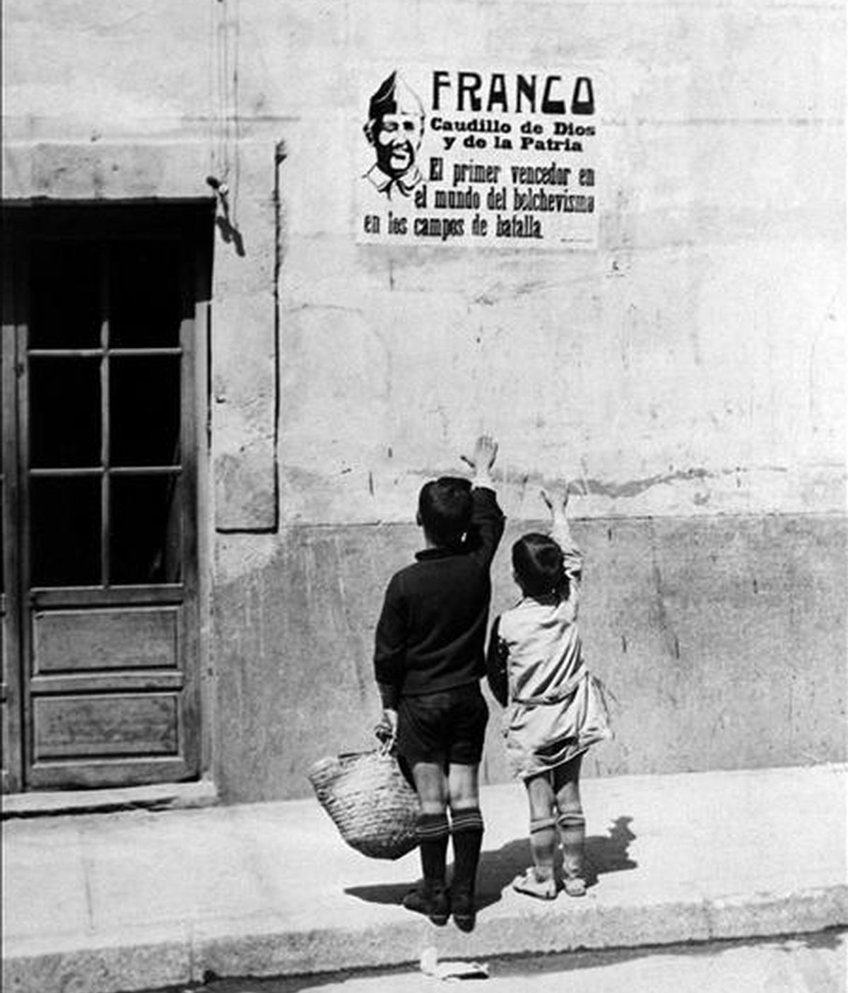 Carteles de Franco en los pueblos españoles al terminar la Guerra Civil. Dos niños alzan los brazos, en saludo fascista, a un cartel con la foto de Franco. EFE/Archivo