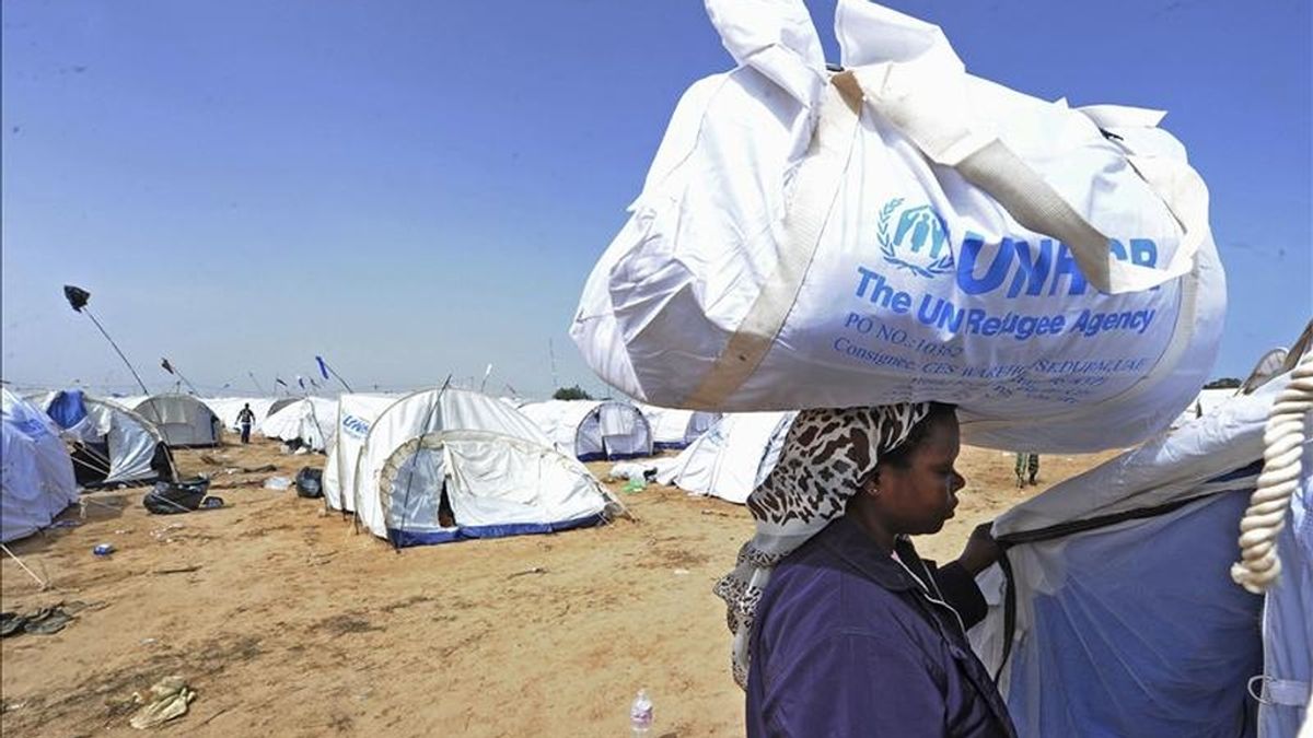 Una refugiada carga ayuda humanitaria en su cabeza, en el campo de refugiados de ACNUR, en el paso de Ras el Jedir, por donde han salido más de 100.000 refugiados del conflicto libio. EFE/Archivo