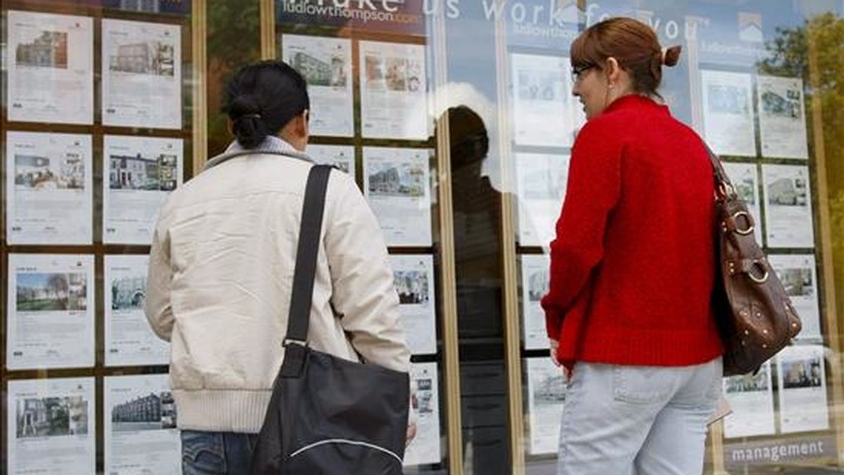 Dos mujeres leen detenidamente un escaparate con carteles de viviendas en venta. EFE/Archivo