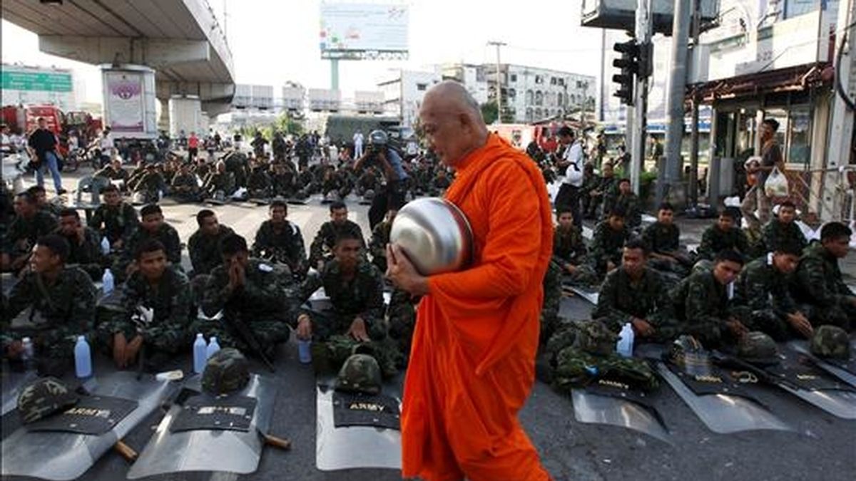 Un monje pasa al frente de varios soldados tailandeses sentados en una de las calles que conduce a la sede del Gobierno en Bangkok. EFE