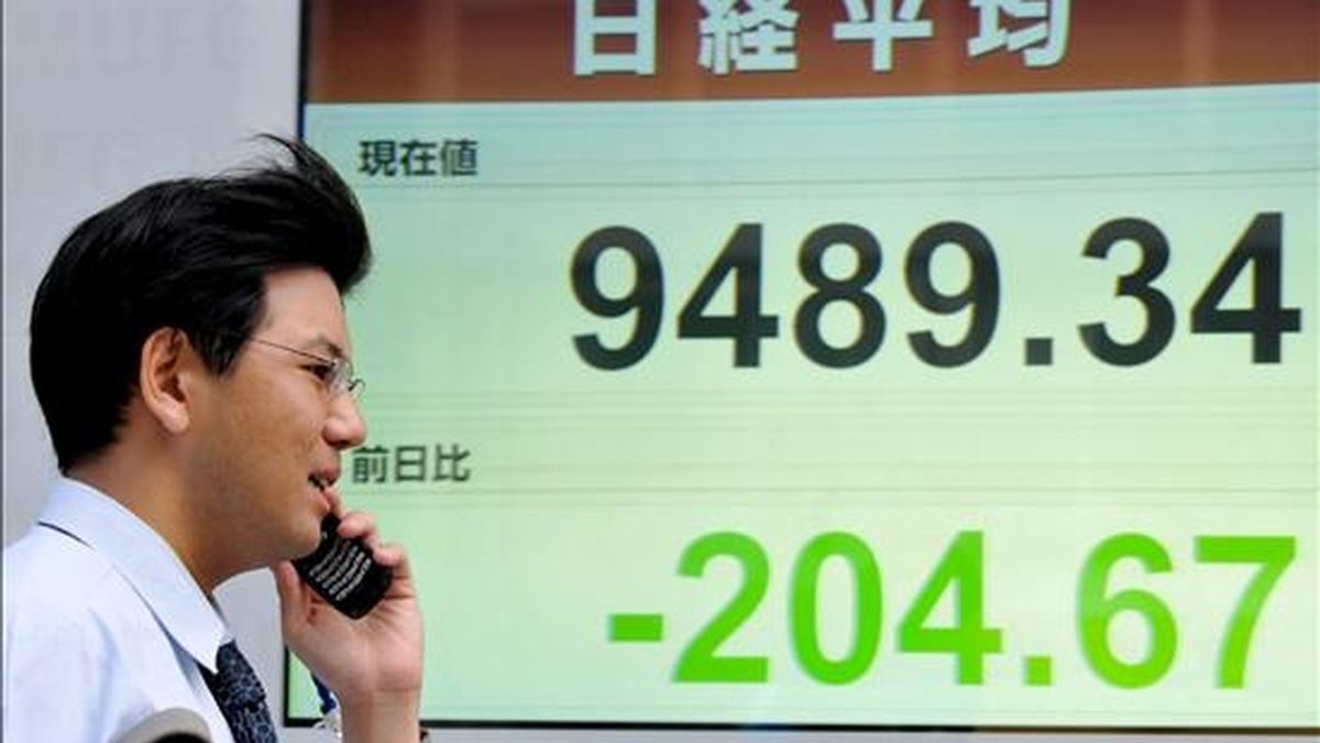 Un empresario japonés que habla por su teléfono móvil pasa junto a un tablero electrónico de la bolsa de valores, en Tokio, Japón. EFE