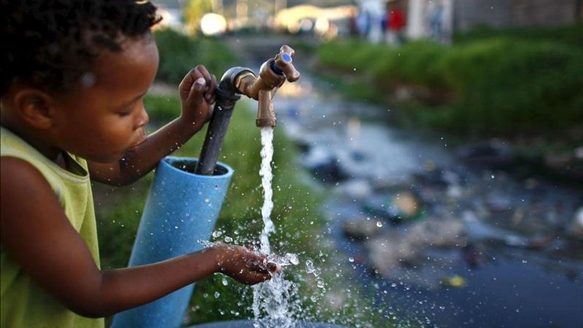 Un niño sudafricano bebe agua de una fuente situada junto a un río contaminado en el asentamiento de Masiphumelele, en Ciudad del Cabo (Sudáfrica). EFE/Archivo