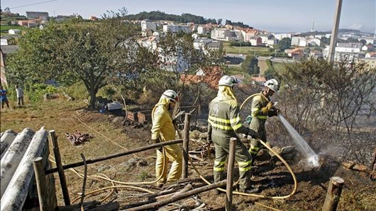 Varios bomberos refrescan una zona afectada por el reciente incendio forestal en Santiago de Artexio, en A Coruña. En otro incendio en esta provincia ha sido hallado hoy el cadáver de una mujer. EFE/Archivo