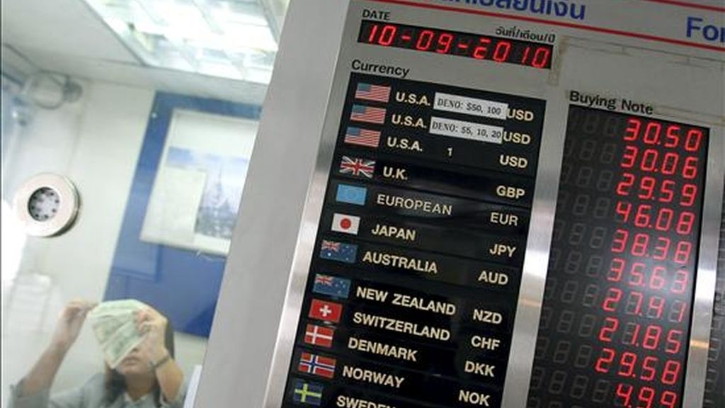 Una mujer (izda) cuenta dinero junto a un letrero informativo de divisas de moneda extranjera en Bangkok. EFE/Archivo