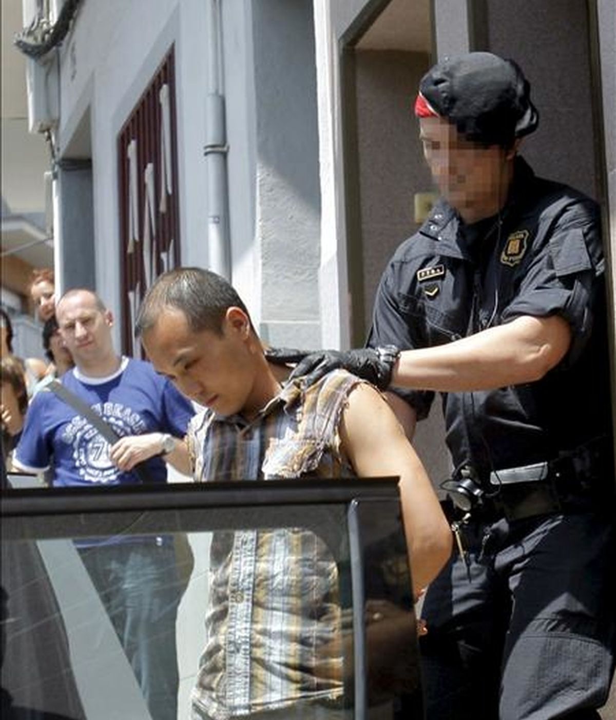 Un agente de los Mossos d'Esquadra traslada a uno de los detenidos durante la operación en la que se han registrado unos 70 talleres clandestinos textiles regentados por ciudadanos de origen chino en Mataró (Barcelona). EFE/Archivo