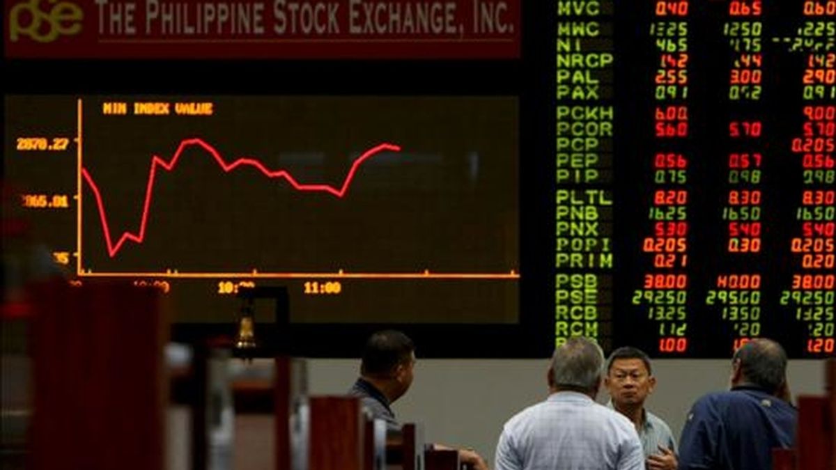 Varios agentes conversan junto a un panel electrónico en el que se muestran las operaciones de Bolsa, en el parqué de Manila. EFE/Archivo