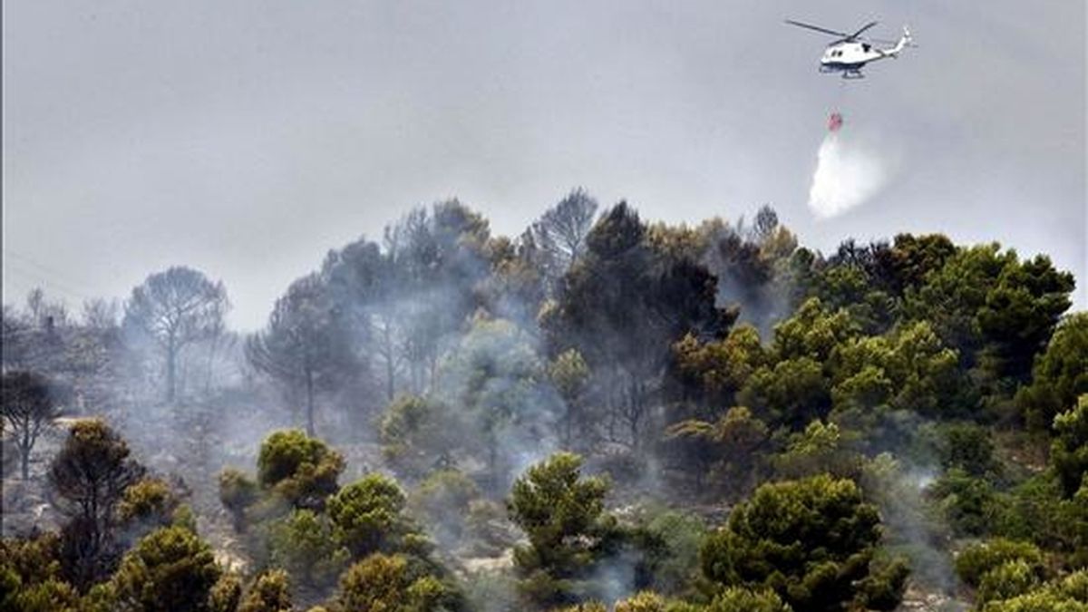 Un helicóptero arroja agua sobre la masa forestal de la montaña de Santa Ana para evitar la semana pasada la propagación de un incendio forestal en el término de Gandía (Valencia). EFE/Archivo