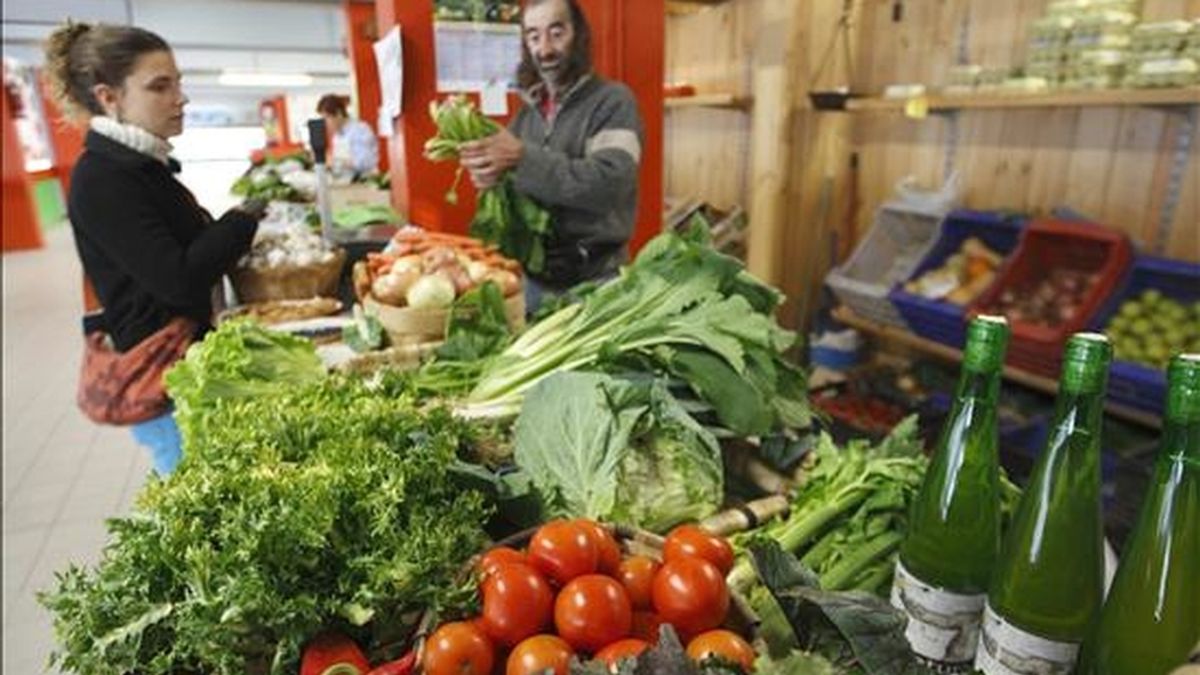 Un comerciante atiende a una clienta en su puesto de verduras en un mercado. EFE/Archivo