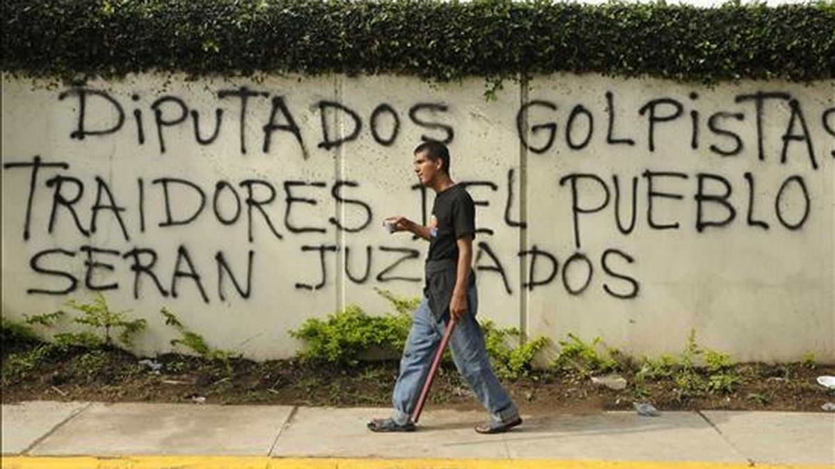 Un manifestante armado con un palo pasa junto a un grafiti en contra del presidente interino de Honduras Roberto Micheletti, cerca a la Casa Presidencial en Tegucigalpa, capital que amaneció con una aparente tranquilidad en las calles tras un toque de queda que duró hasta las 06.00 horas (12.00 GMT). EFE