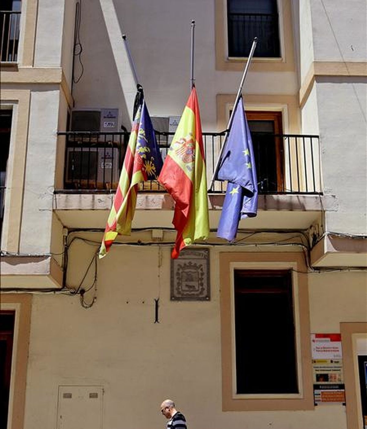 Un vecino pasa bajo las banderas a media asta situadas en la fachada del ayuntamiento de Navarrés, localidad valenciana de donde era natural María José Such, fallecida en un accidente de autobús en la región peruana de Cuzco. EFE