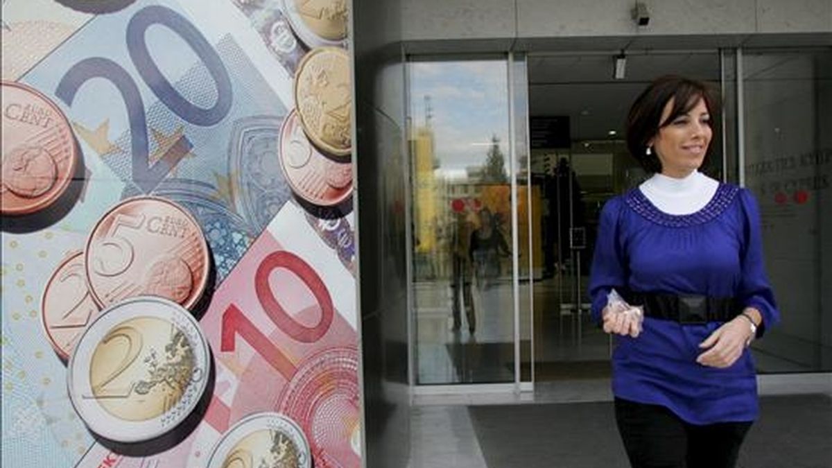 Una mujer camina junto a una valla publicitaria con monedas y billetes de euro. EFE/Archivo