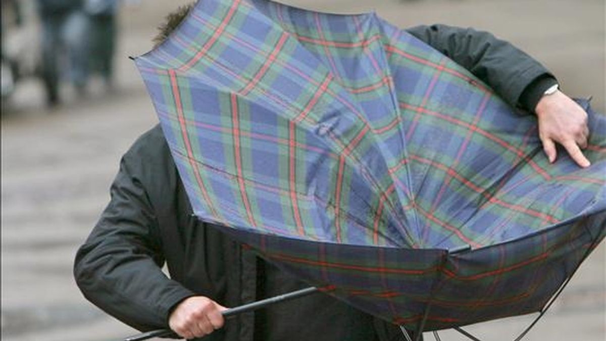 Un hombre trata de arreglar su paraguas, vuelto del revés por una ráfaga de viento. EFE/Archivo