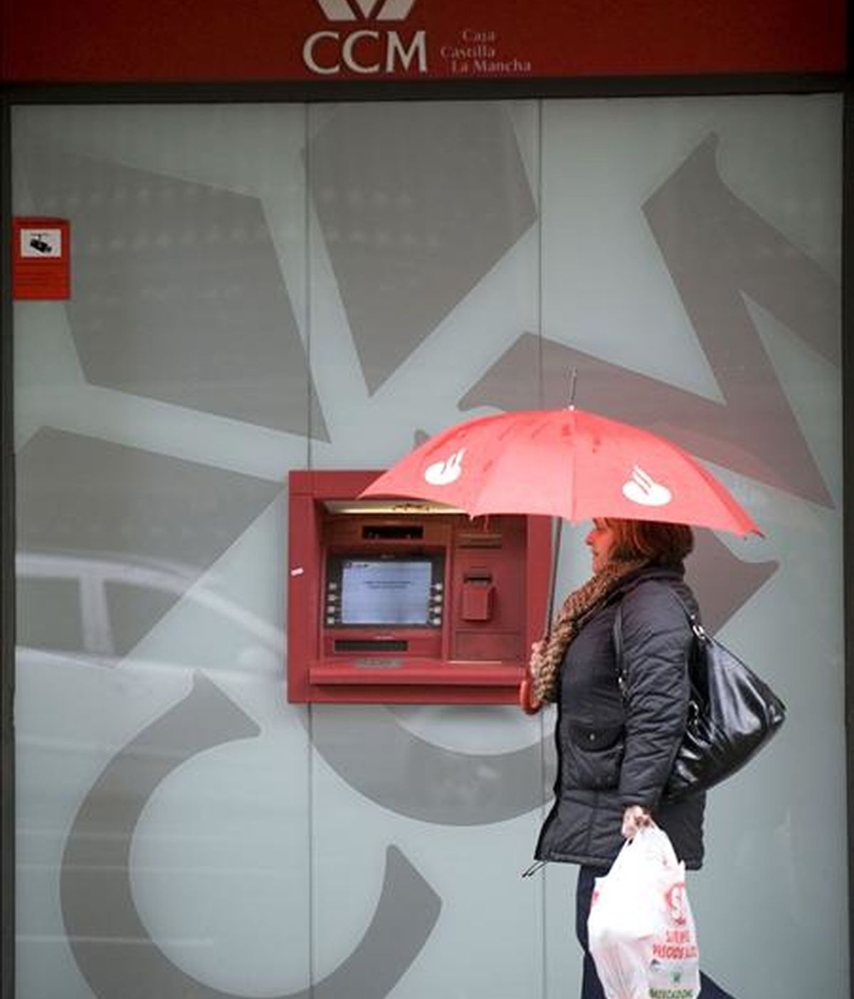 Una mujer con un paraguas pasa delante de un cajero automático. EFE/Archivo