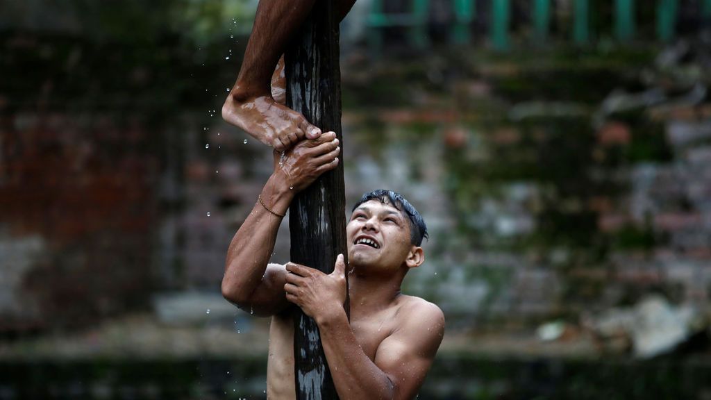 Un hombre ayuda a uno de sus compañeros a subir un poste de madera en Khokana, Nepal