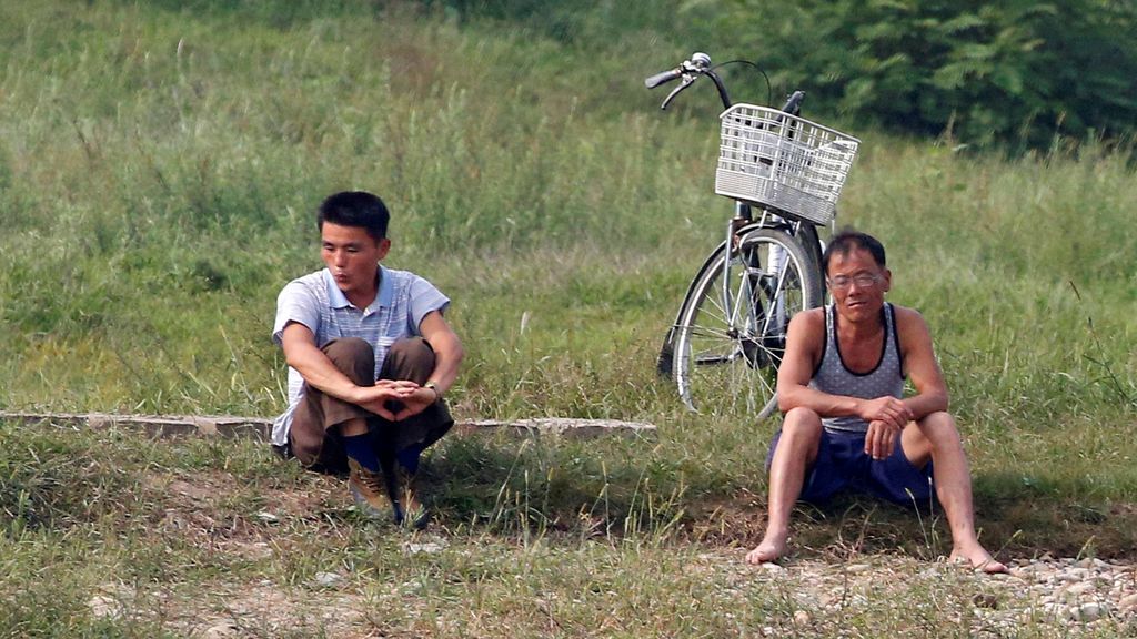 Hombres norcoreanos se encuentran sentados en un banco en el Río Yalu