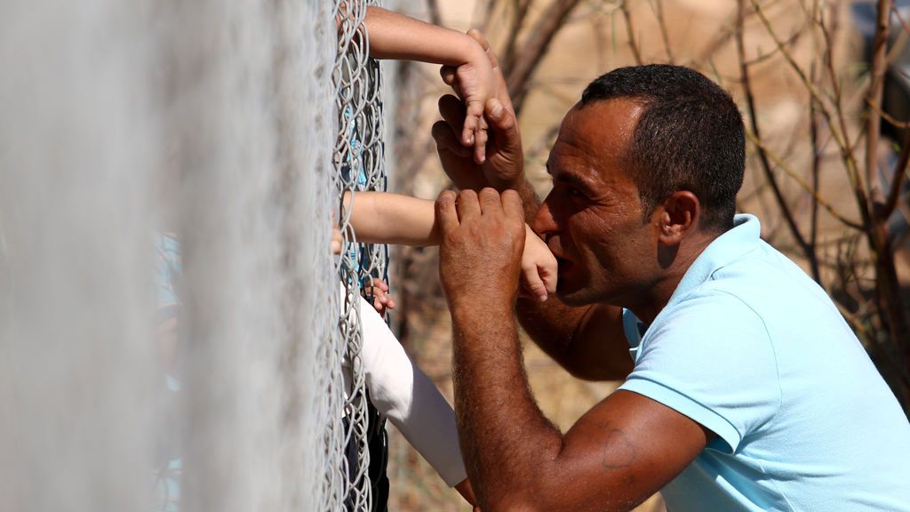 Un hombre sirio besa las manos de sus hijos que llegaron al campamento de refugiados de Kokkinotrimithia
