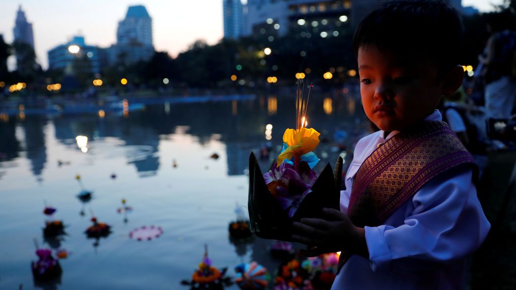 Un niño vestido con ropa tradicional tailandesa se prepara para colocar una canasta flotante en un estanque
