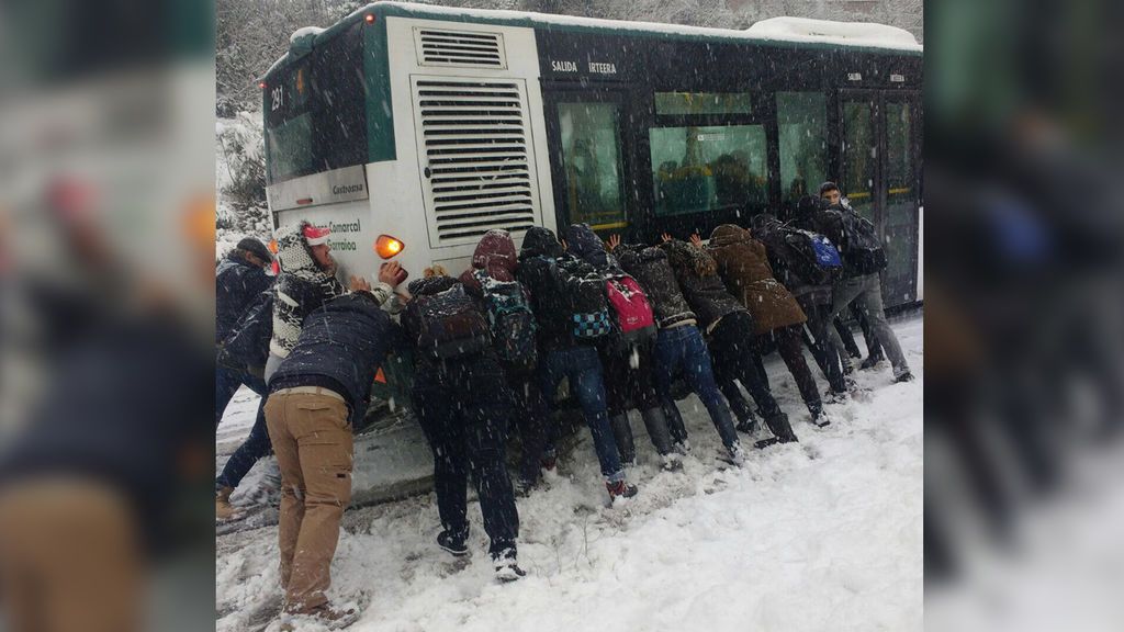 Un grupo de personas empuja a un autobús atrapado por la nieve en Pamplona