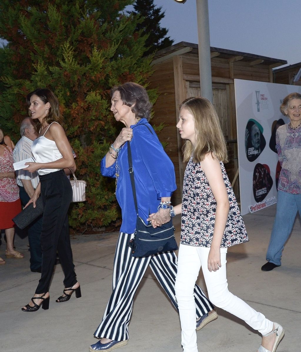 Doña Sofía, con una camisa llamativa de color azul y pantalón a rayas, entra de la mano de Leonor