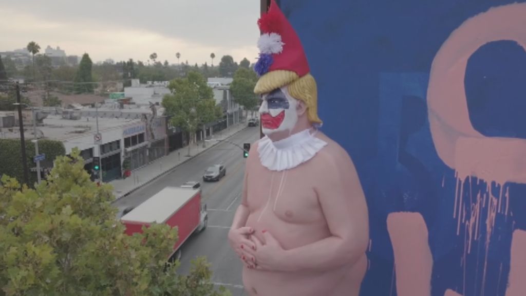 Acción contra Trump: desnudo, vestido de payaso y colgado de una valla publicitaria