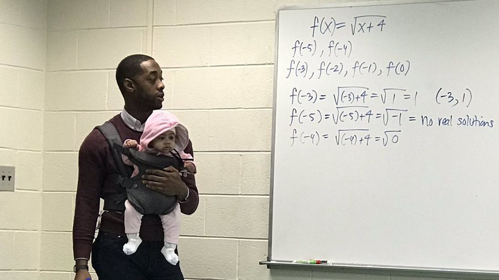 Un profesor imparte su clase mientras sostiene al bebé de un alumno