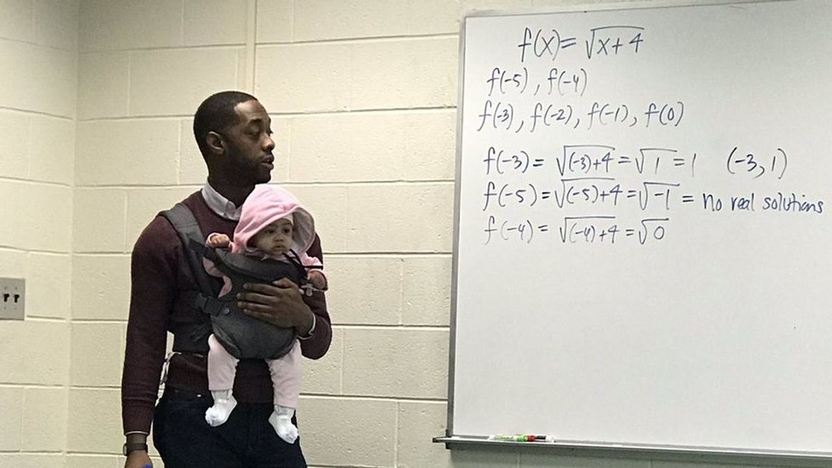 Un profesor imparte su clase mientras sostiene al bebé de un alumno