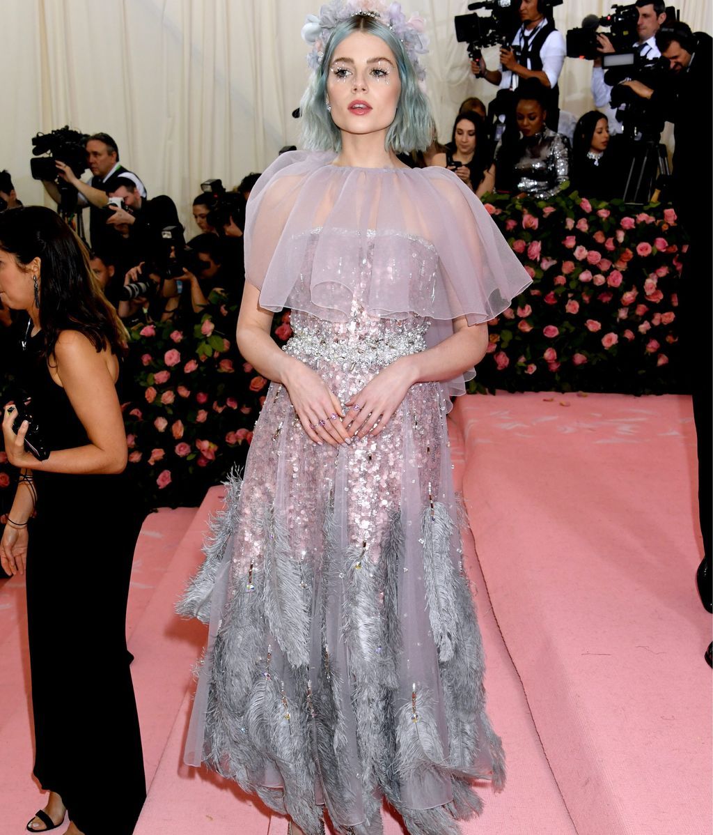 Lucy Boynton con el pelo azul cielo y un vestido de plumas y lentejuelas
