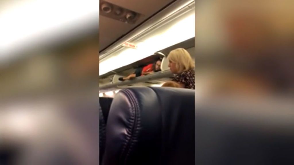 Una azafata recibe a los pasajeros del avión metida en uno de los maleteros