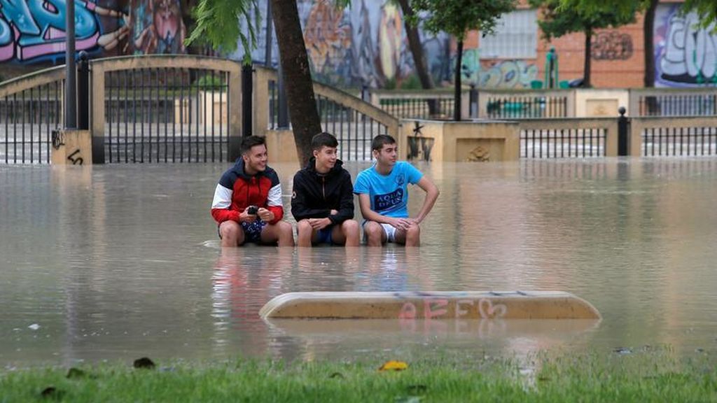 Niños se sientan en un banco en un parque cerca del desbordante río Segura mientras las lluvias torrenciales azotan Orihuela