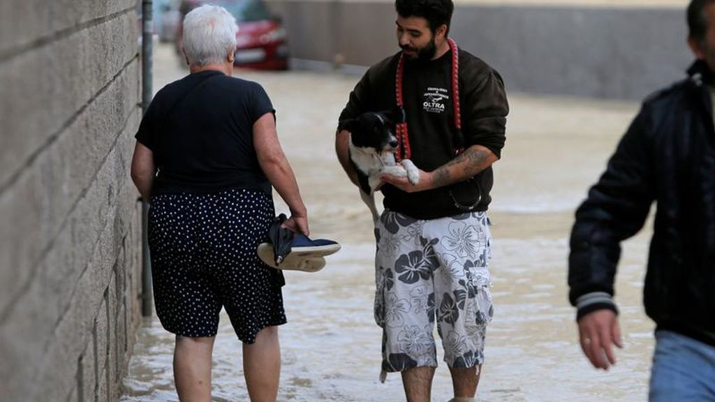 Un joven camina con su perro en brazos por una calle totalmente inundada en Orihuela