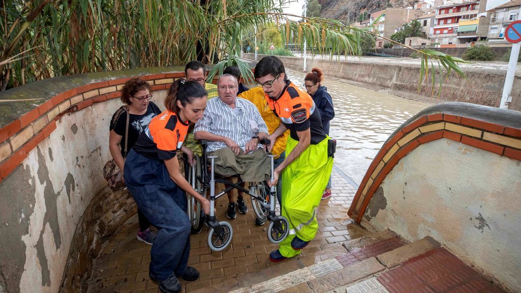 Voluntarios de protección civil trasladan a un hombre en silla de ruedas tras las intensas lluvias esta tarde en Murcia