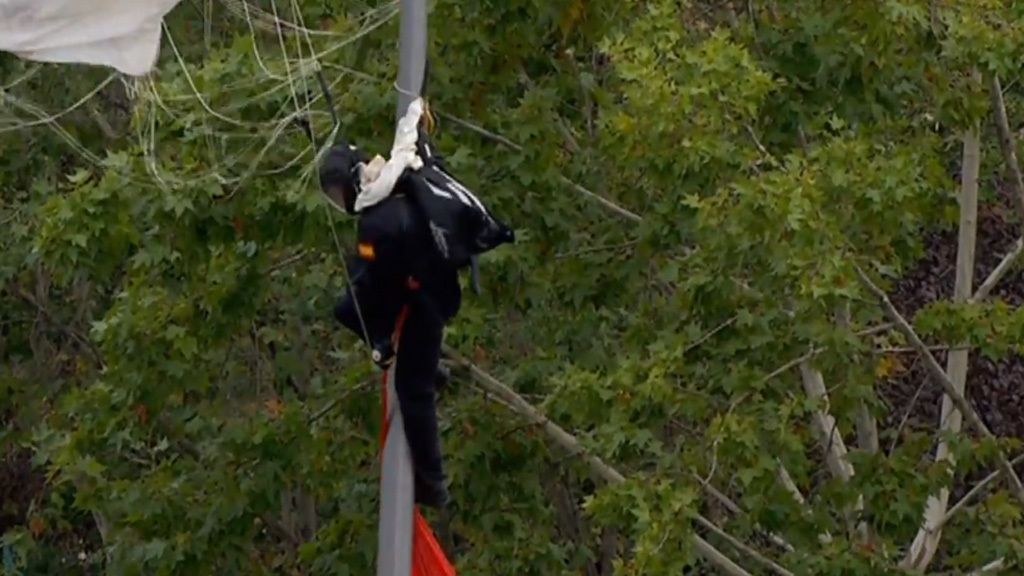 Desfile del Día de la Hispanidad: El paracaidista que lleva la bandera se engancha a una farola