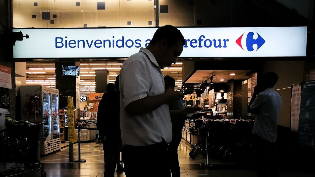 Un hombre mira un papel ante la puerta de un supermercado