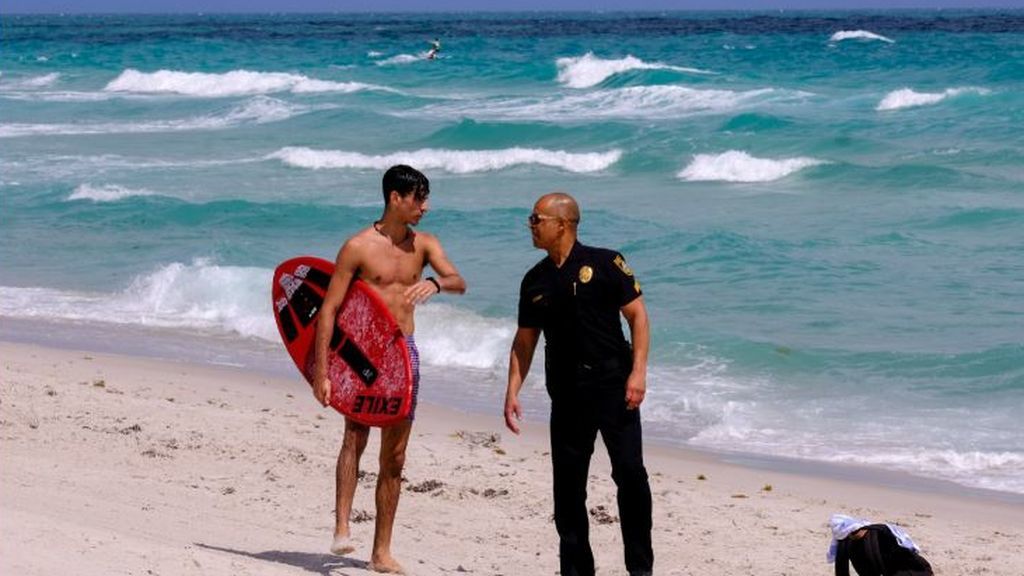 Un policía informa a un surfero que la playa está cerrada por el COVID-19