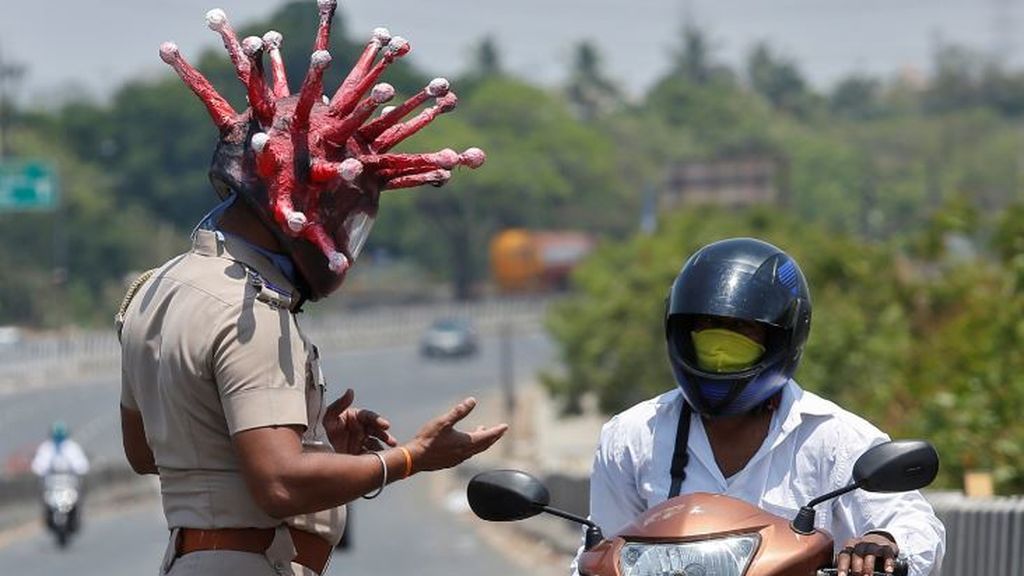 En Chennai, ciudad india, un policía con un casco que representa al coronavirus conmina a un motorista a respetar el confinamiento